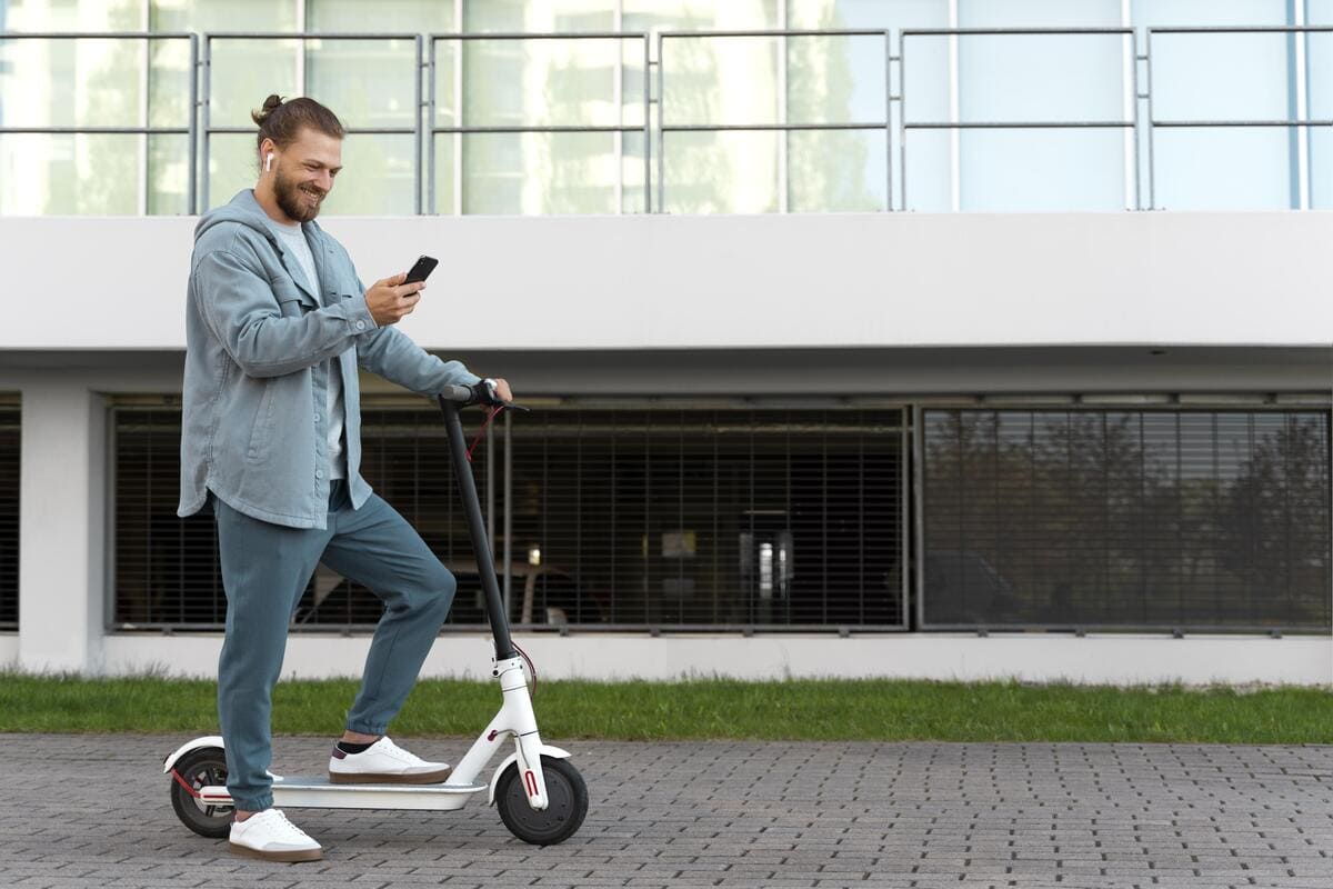 A man stands on a scooter, focused on his phone while balancing on the moving vehicle.
