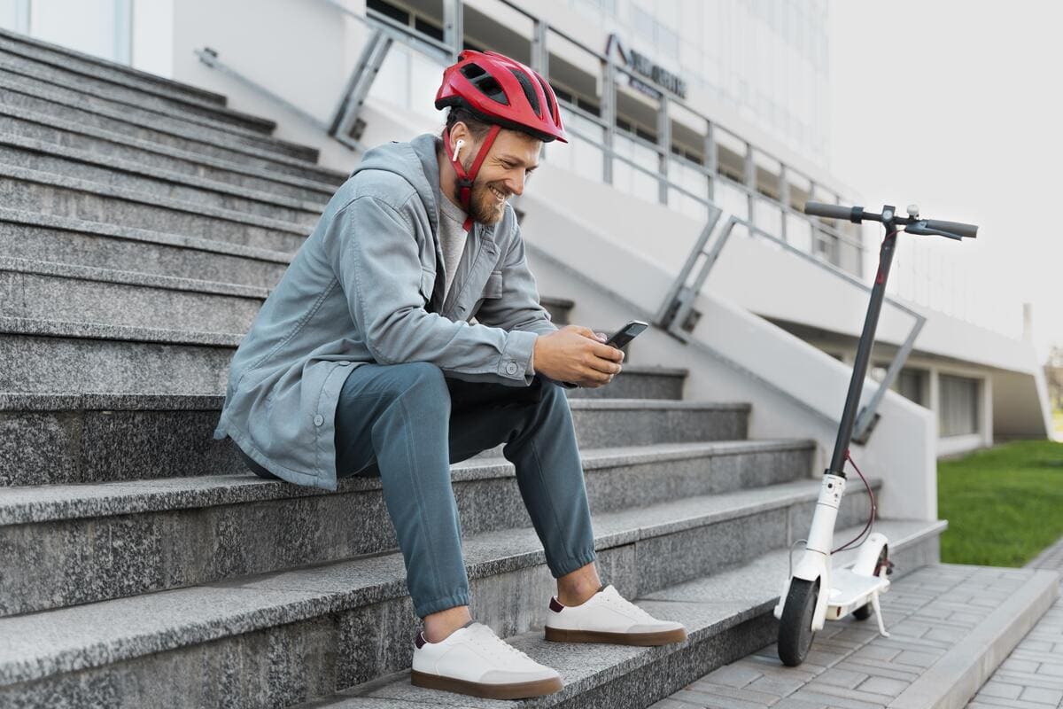 A man wearing a helmet sits on steps next to a scooter, looking relaxed and enjoying the moment.