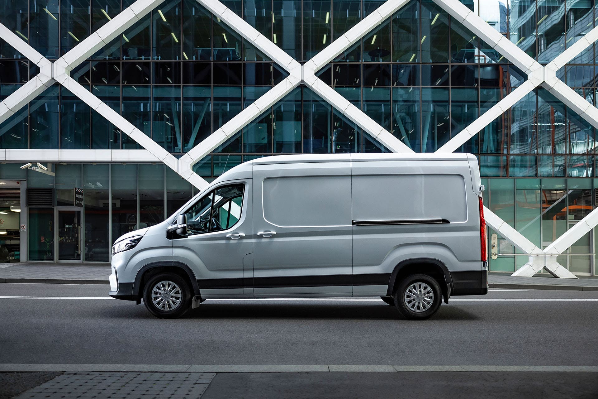 A new Ford Transit van parked in front of a large modern building, showcasing its design and size.