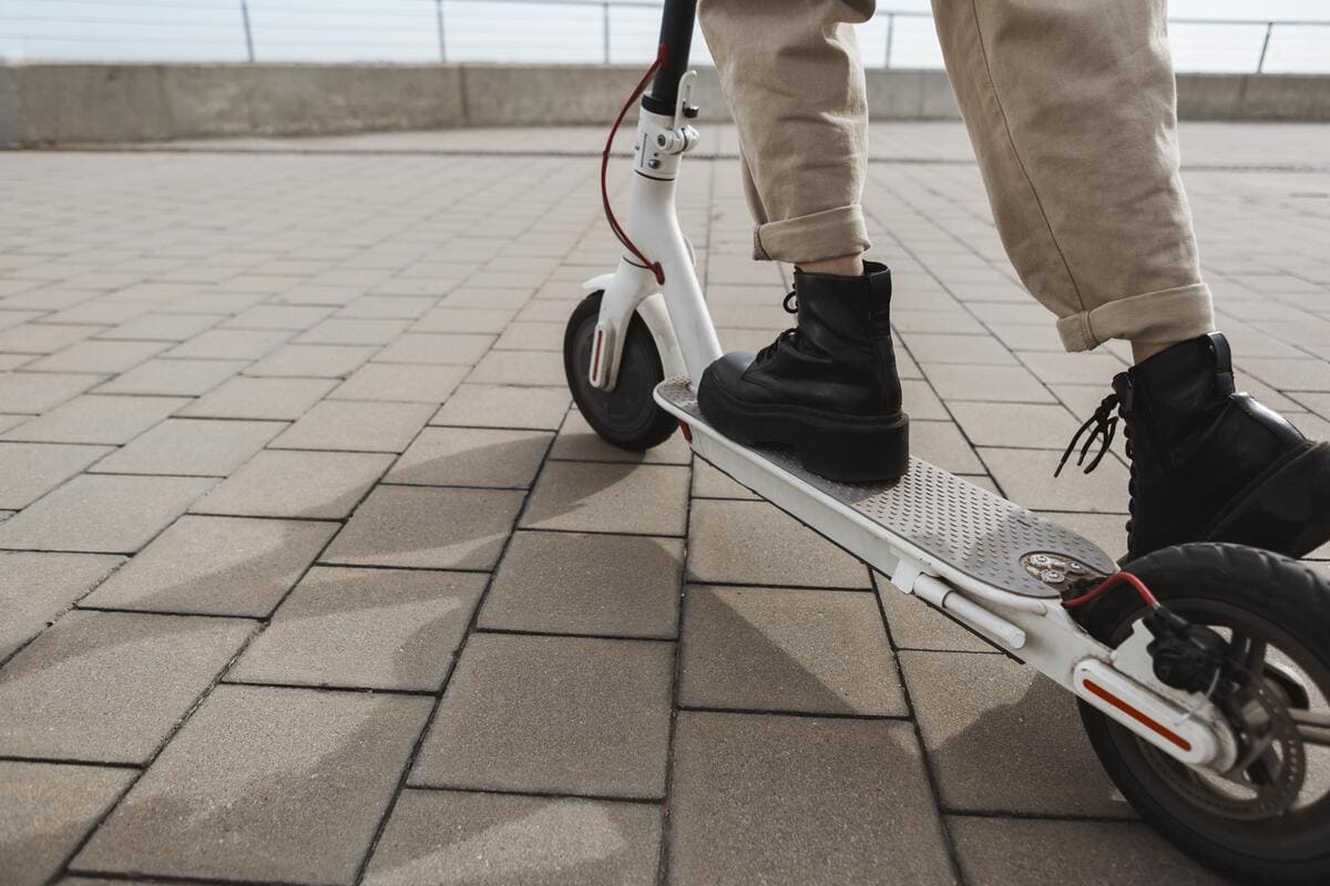A person riding a white electric scooter on a city street, wearing a helmet and casual clothing.