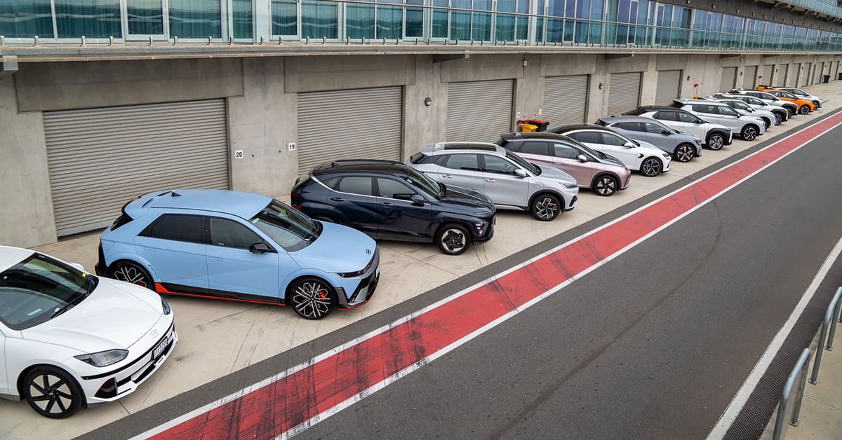 A row of cars parked on a track featuring a prominent red stripe alongside them.