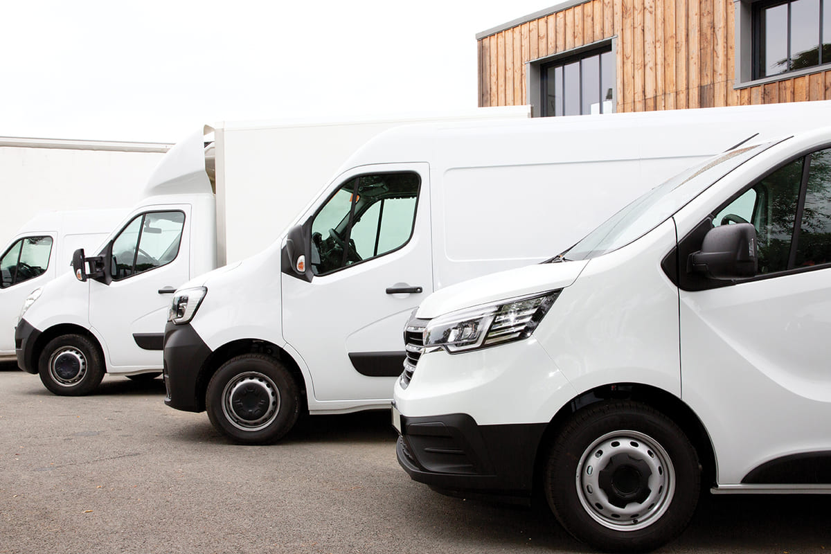 A row of white vans parked neatly in front of a building under a clear blue sky.