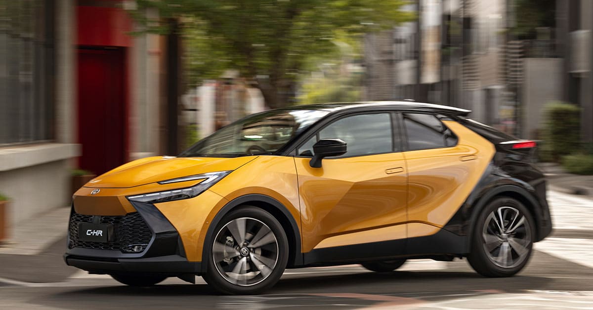 A Toyota C-HR drives along a bustling city street, showcasing its sleek design and urban versatility.