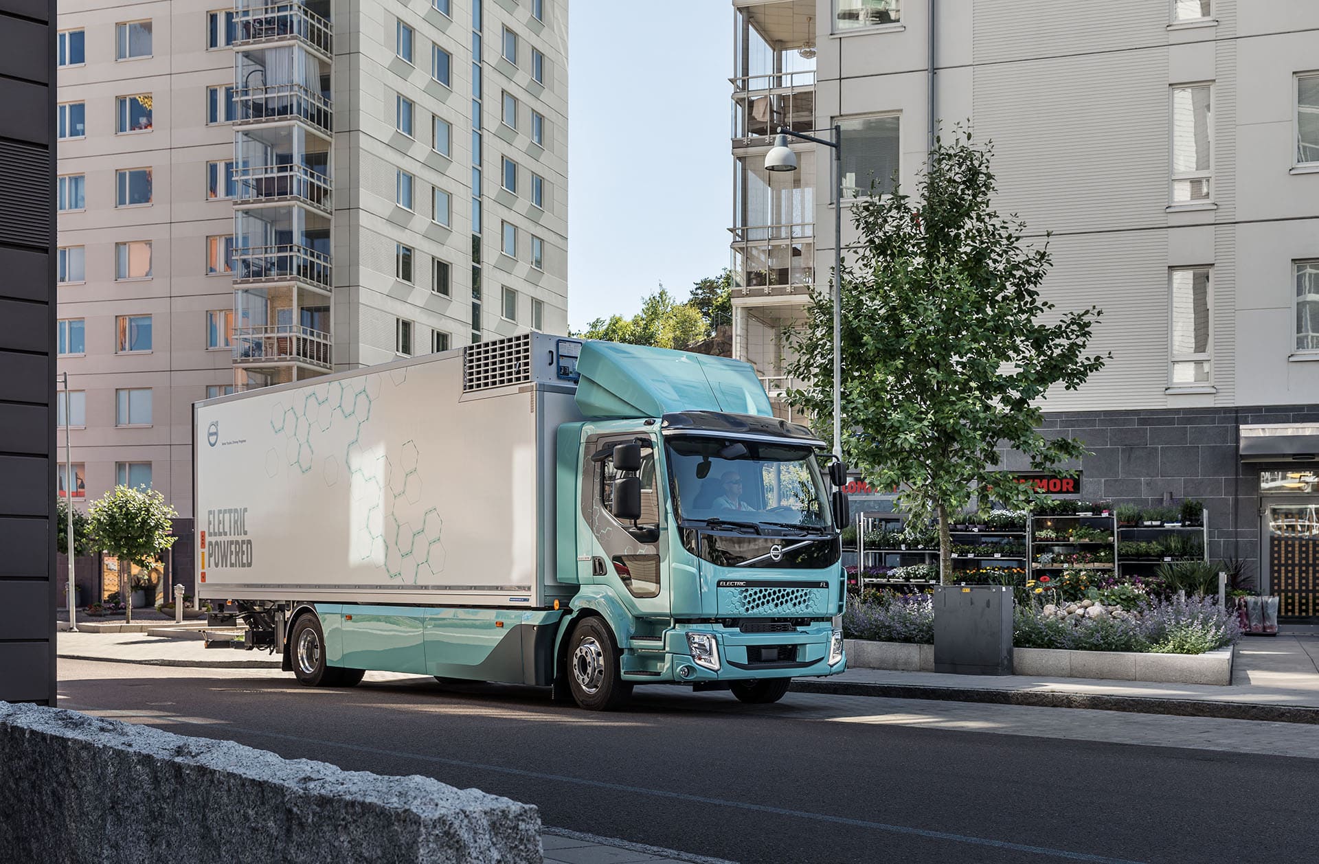 A truck driving along a busy city street, surrounded by buildings and pedestrians.