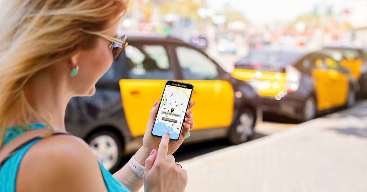 A woman checks a taxi app on her cell phone while standing on a city street.