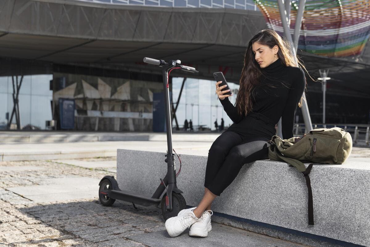 A woman sitting on a bench, looking at her phone, with trees and a park path in the background.