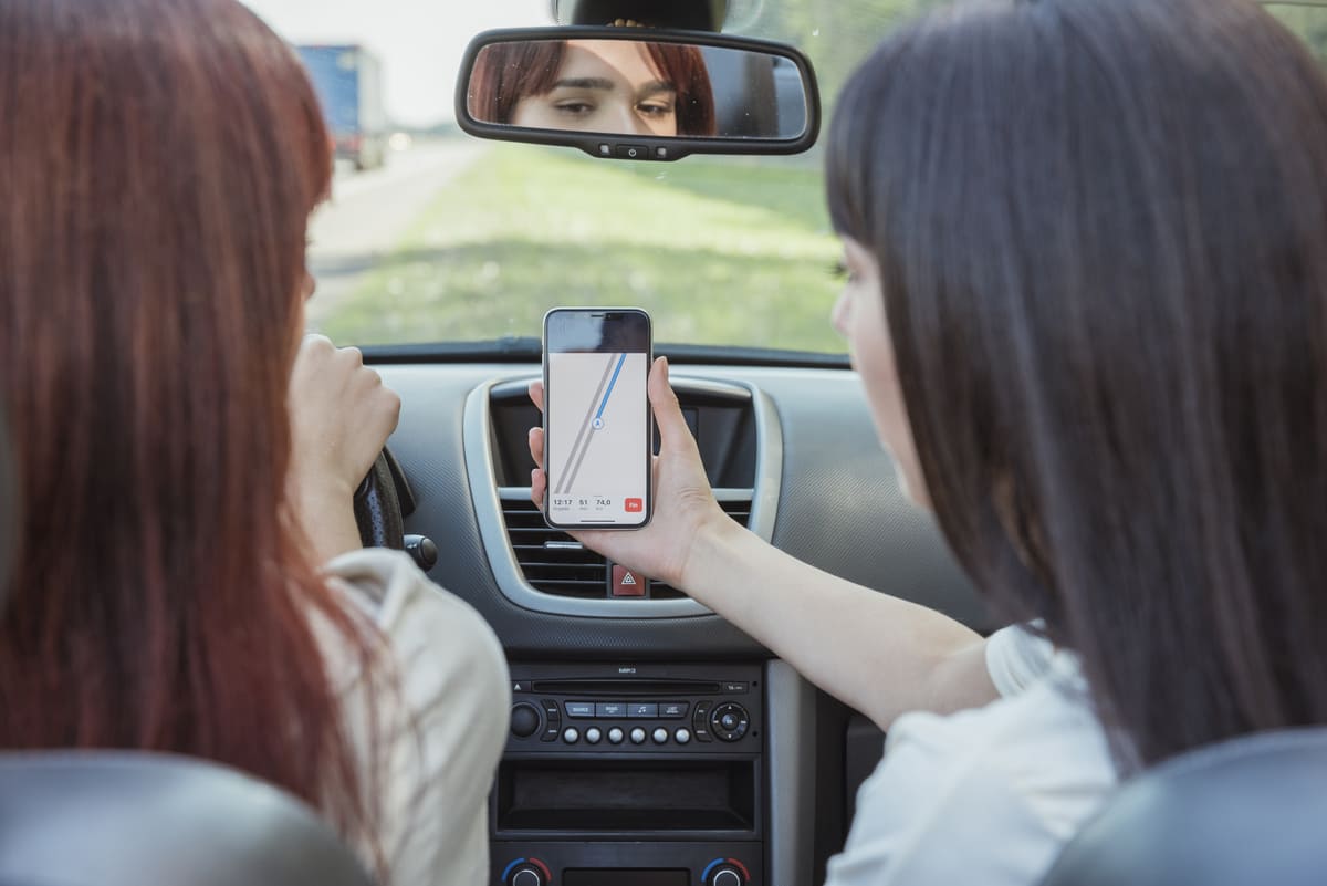 Two women in the back seat of a car, focused on their phones, with soft lighting and casual expressions.